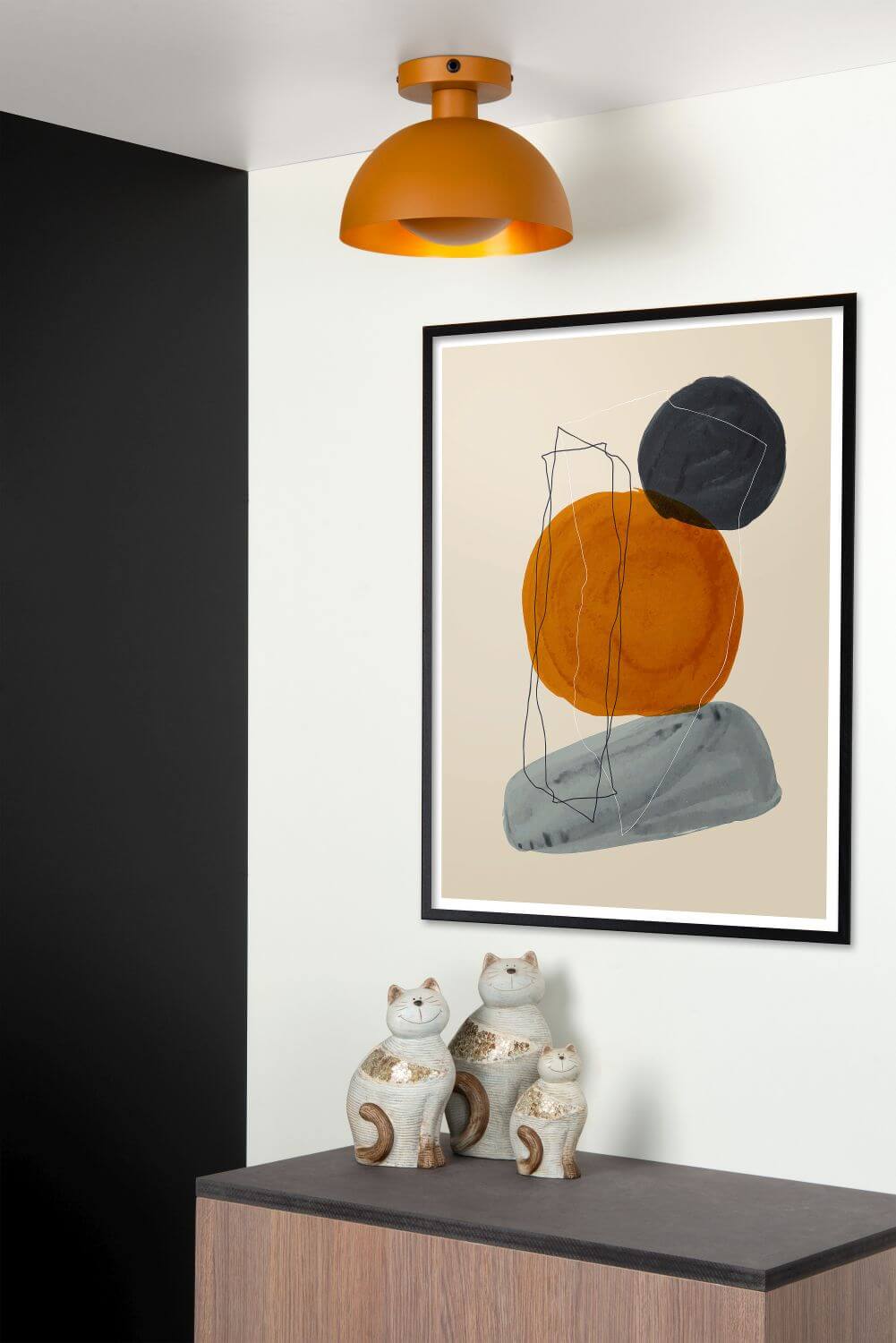 Plafonnier jaune allumé dans un intérieur moderne, tableau abstrait et trois céramiques de chats.