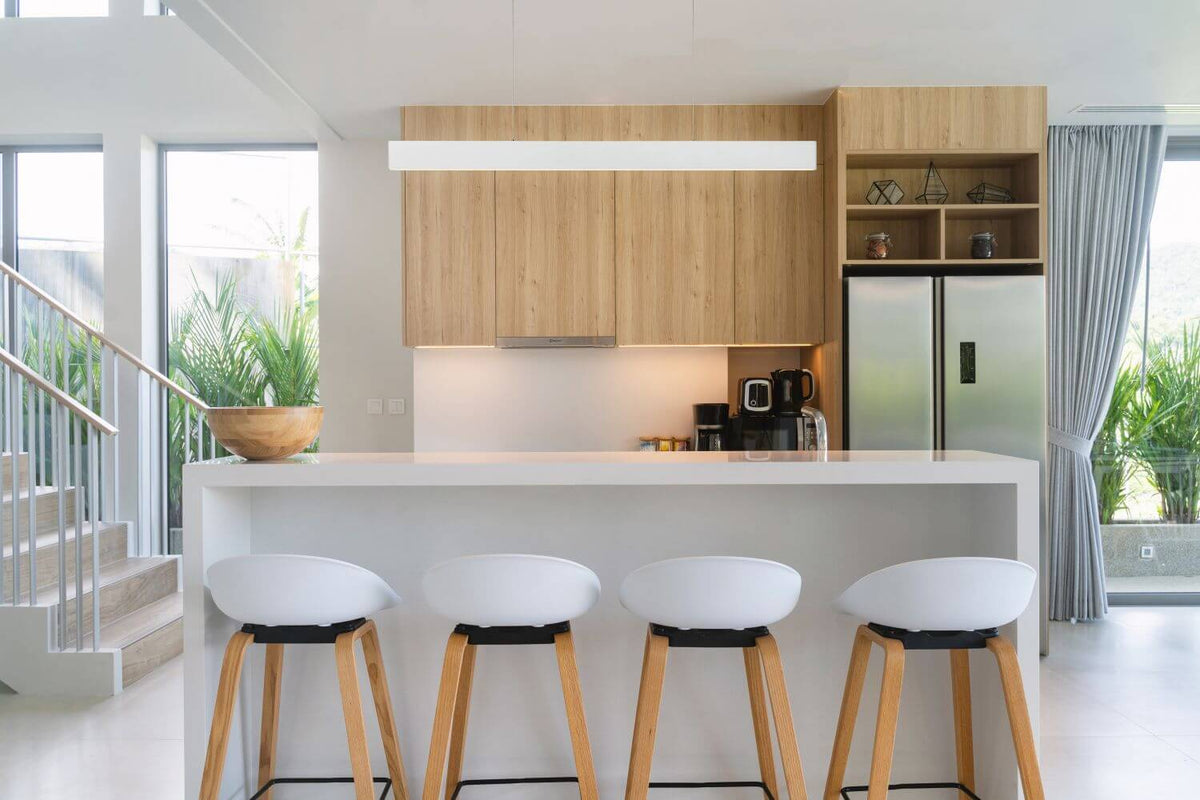 Suspension blanche rectangulaire éclairant un plan de travail dans une cuisine moderne en bois clair.