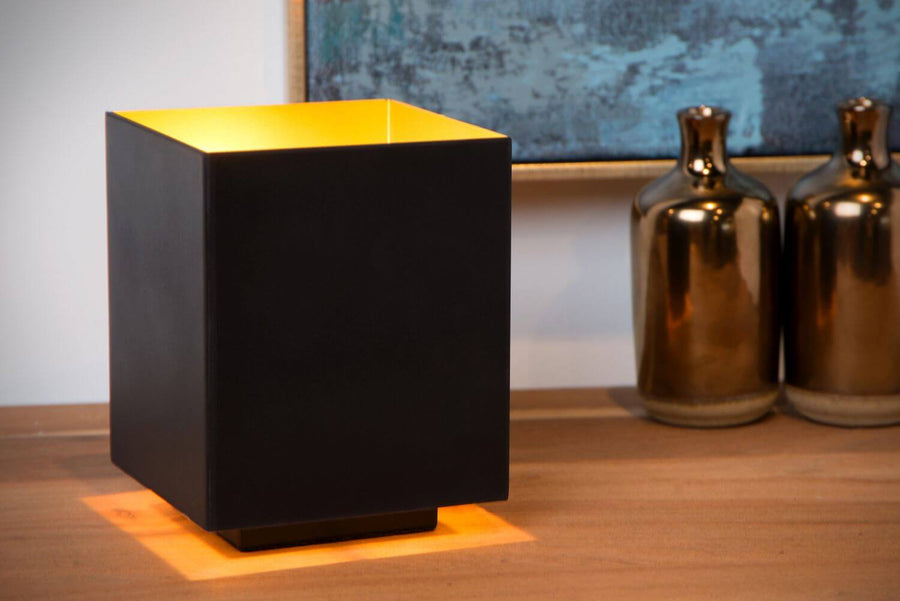 Vue rapprochée de la lampe carrée noire, intérieur doré, posée sur buffet en bois.