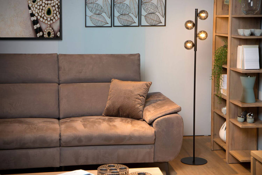 Vue rapprochée du lampadaire aux globes fumés allumés devant un canapé taupe et un coussin.
