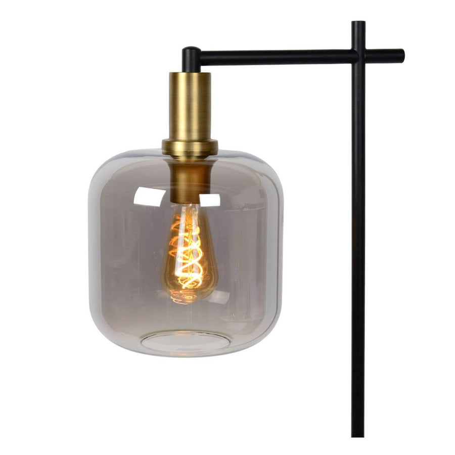 Gros plan sur l'abat-jour en verre fumé et la douille en laiton, ampoule vintage allumée.
