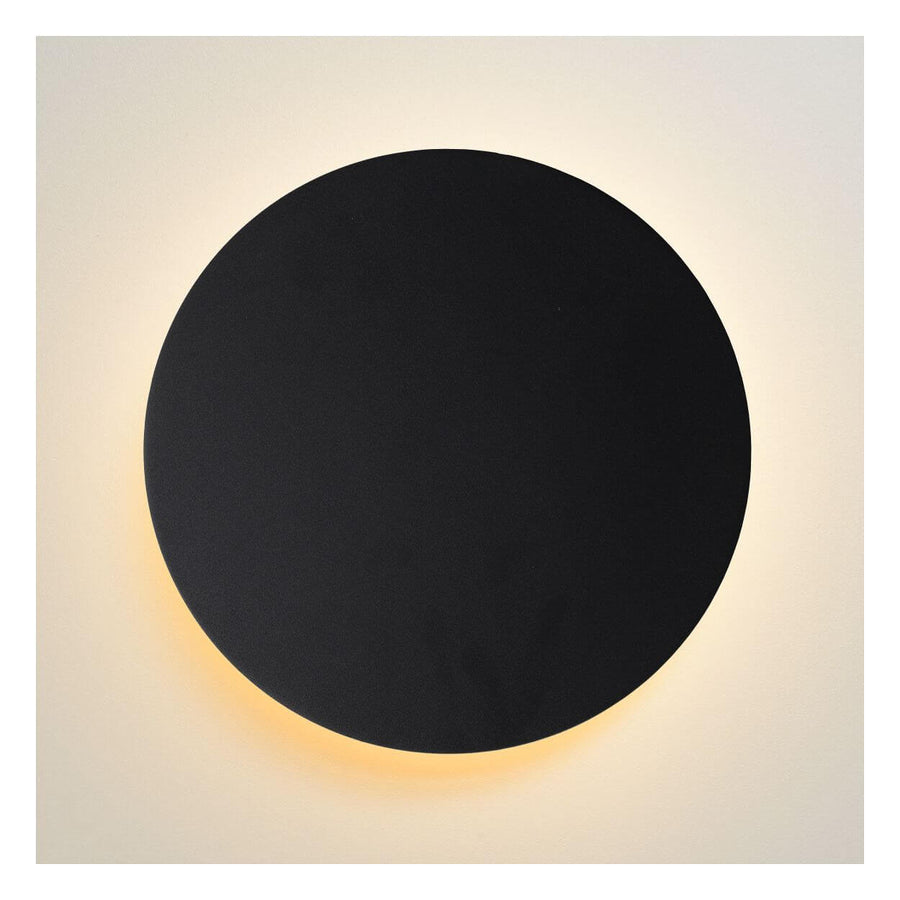 Produit de face allumé, disque noir diffusant une lumière chaude sur mur beige