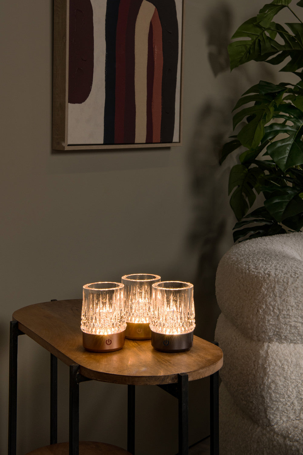 Trois lampes à poser cuivrées allumées sur une table basse en bois, décor intérieur chaleureux.