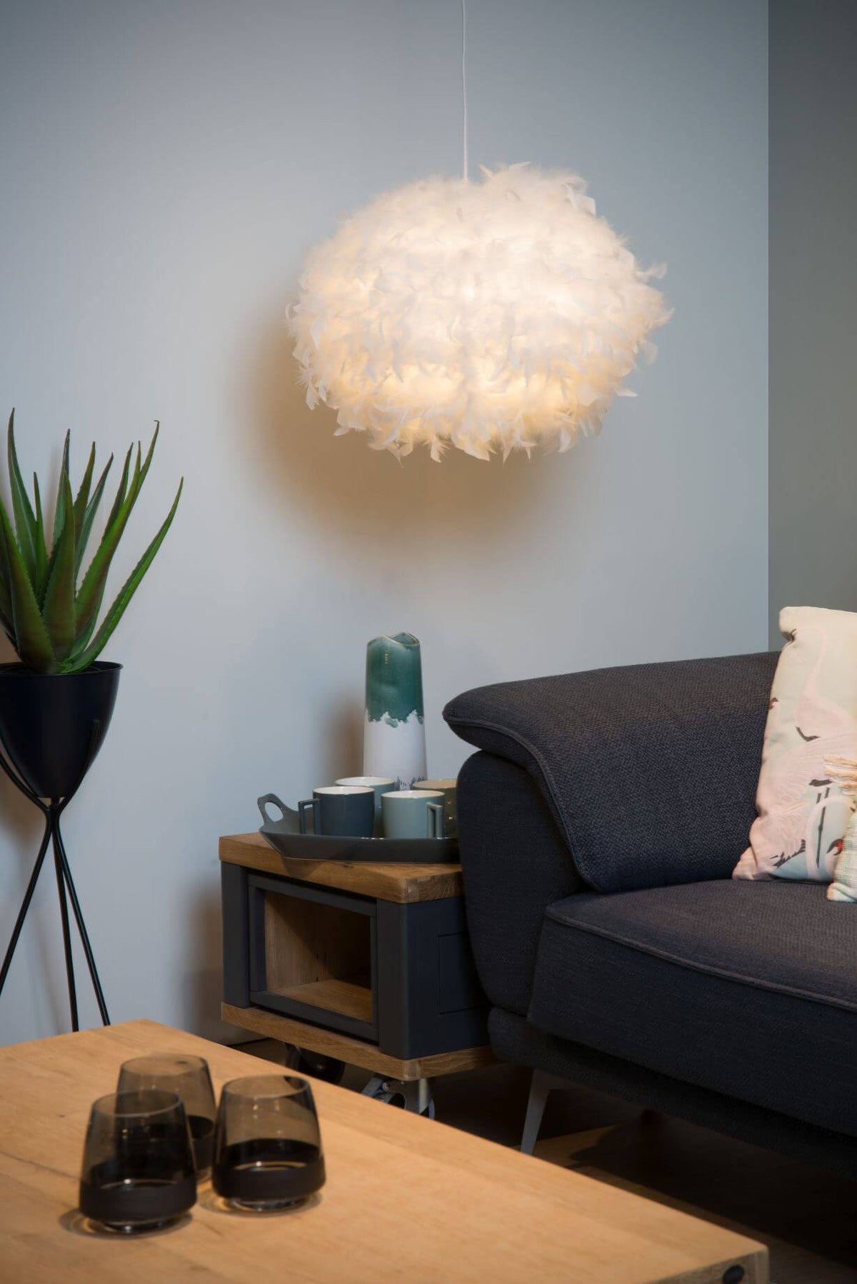 Suspension en plumes allumée au-dessus d'un coin salon avec canapé gris et plante verte.