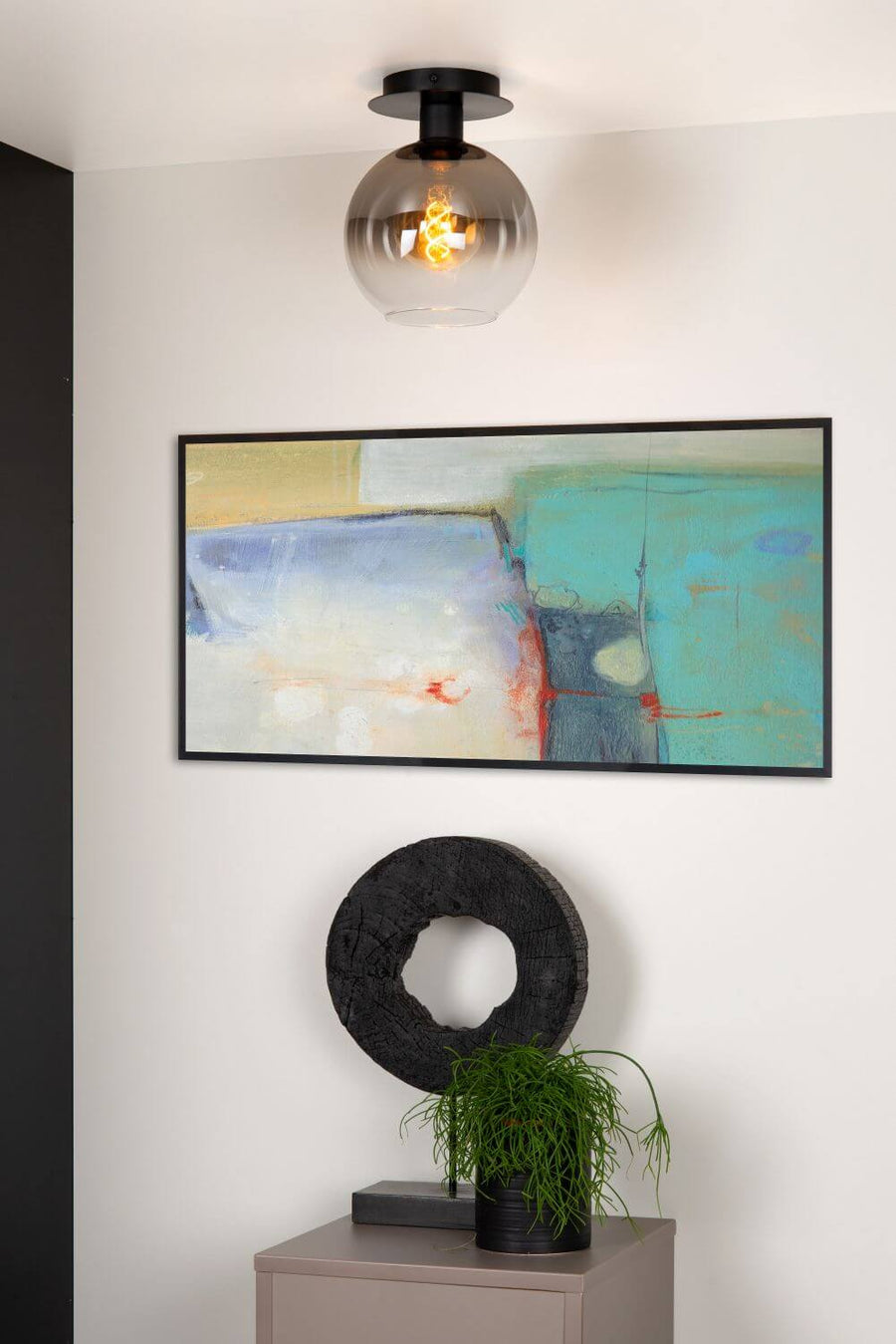 Vue rapprochée du luminaire allumé dans un intérieur, avec tableau abstrait et objets décoratifs.