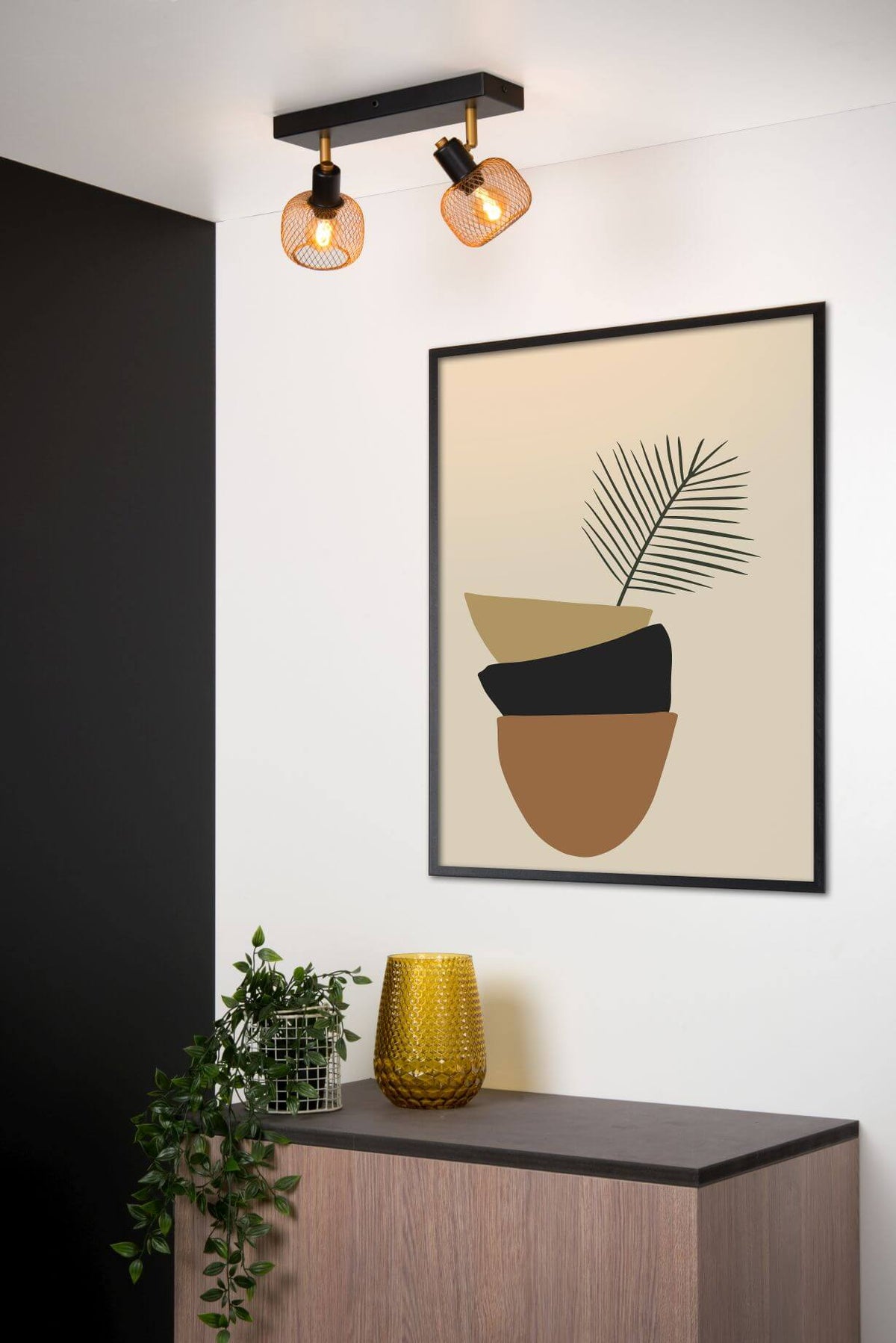Mise en ambiance du plafonnier allumé devant une affiche encadrée et une plante verte