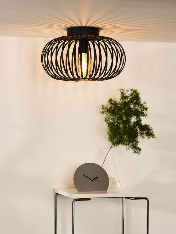 Plafonnier noir allumé au plafond dans un intérieur, table avec horloge et vase.