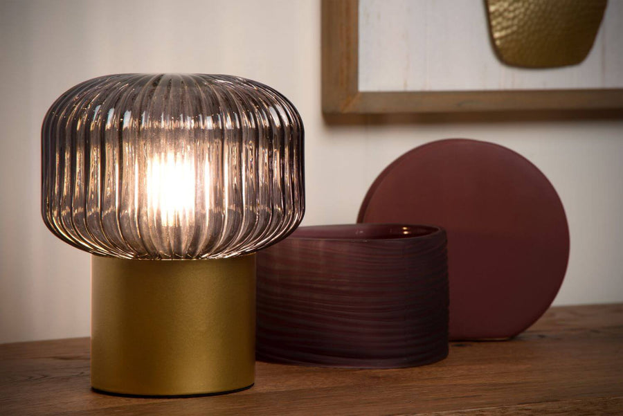 Vue rapprochée du luminaire allumé, abat-jour en verre fumé côtelé sur socle doré