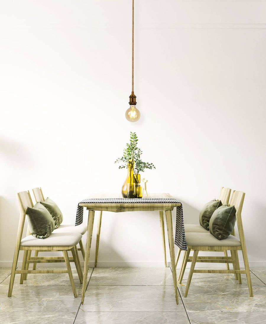 Suspension éclairée au-dessus d'une table à manger en bois avec chaises et décor végétal.