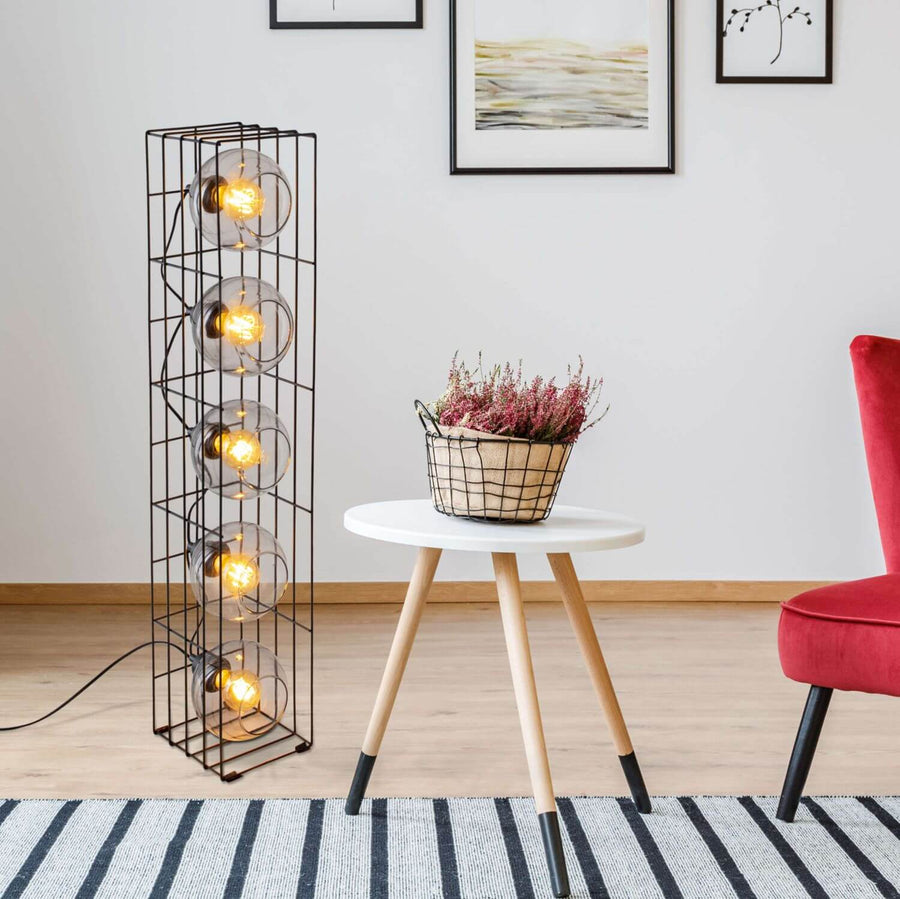 Lampadaire allumé dans un salon avec table blanche, plante, chaise rouge et tapis rayé.