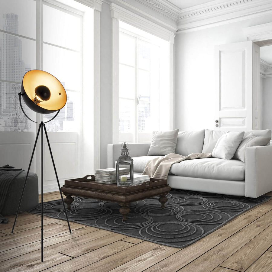 Lampadaire noir et doré dans un salon blanc lumineux avec grandes fenêtres et canapé.