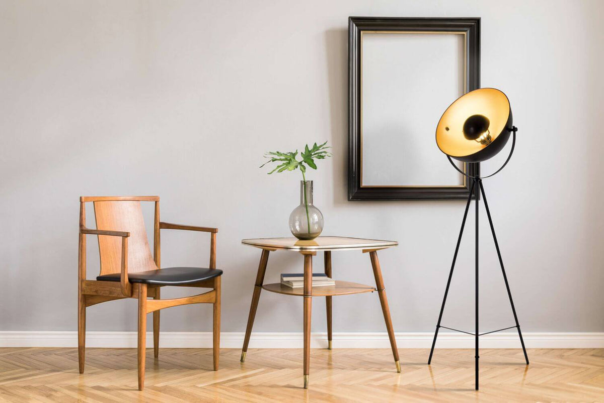 Lampadaire à trépied près d'une chaise en bois, d'une table et d'un miroir mural.