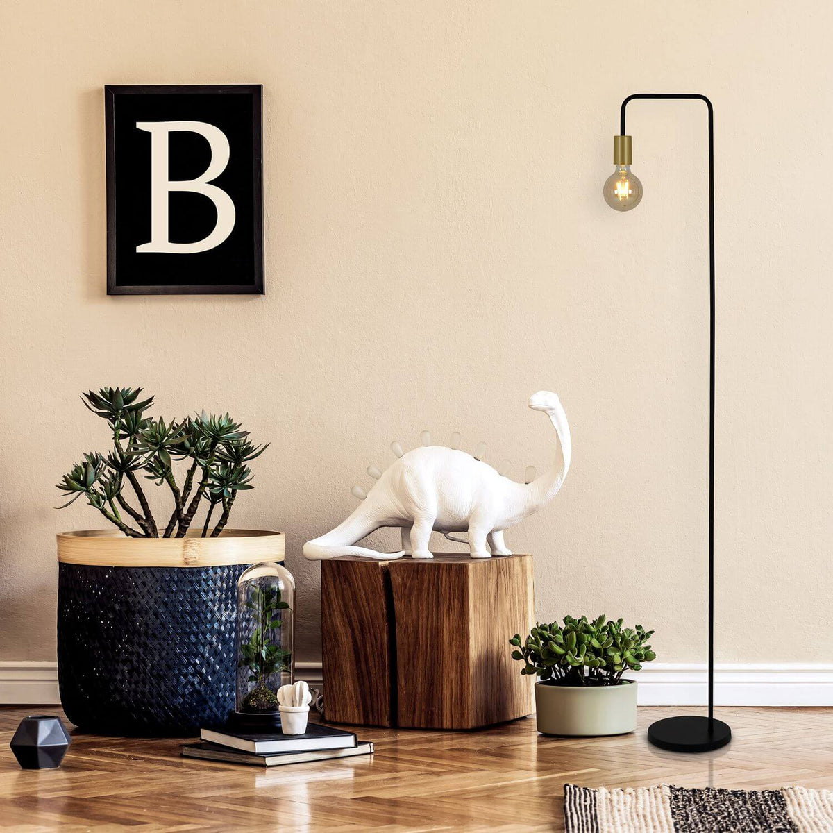 Ambiance déco avec plante, dinosaure blanc, cadre B et lampadaire noir allumé.