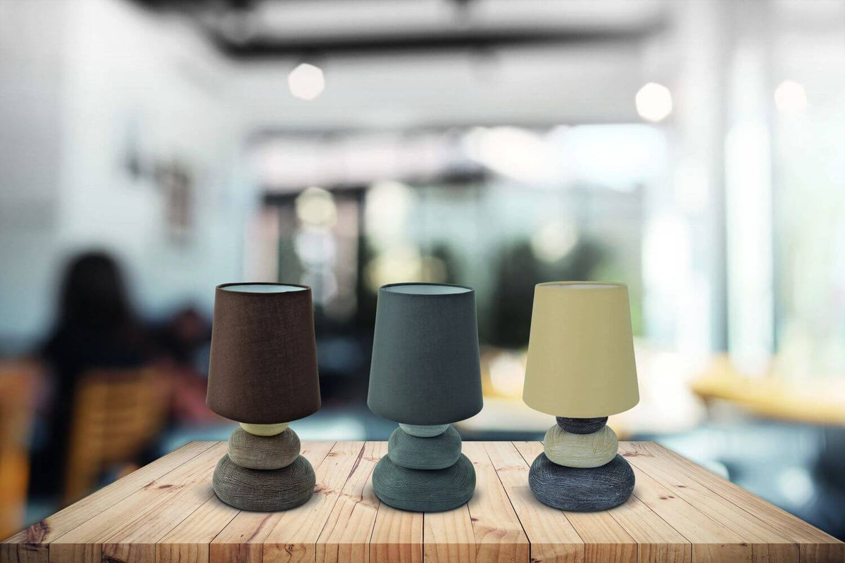 Trois lampes de coloris différents posées sur une table en bois, arrière-plan flou.