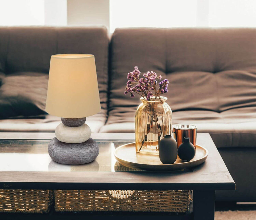 Lampe posée sur une table basse devant un canapé, vase et fleurs séchées.
