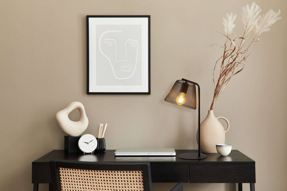 Lampe allumée sur un bureau en bois noir, décor vase et cadre