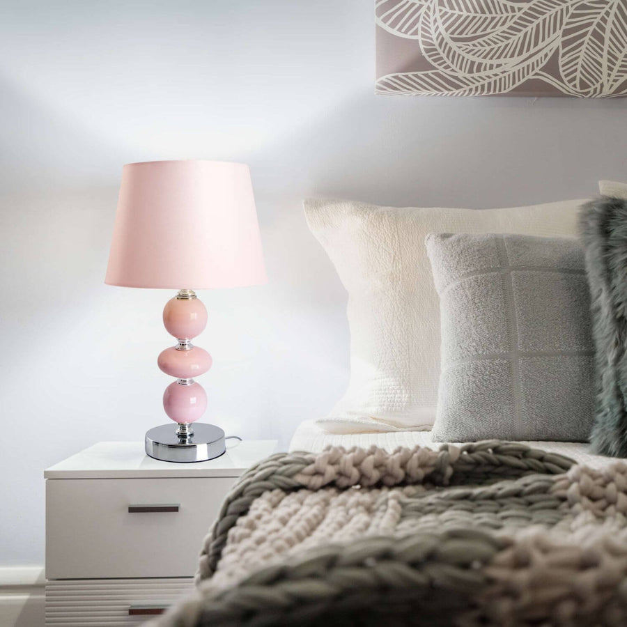 Lampe rose allumée posée sur une table de nuit blanche près d'un lit