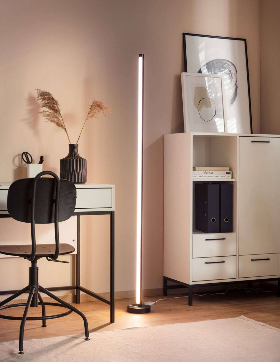Lampadaire en lumière chaude dans bureau épuré, mur beige, meubles et cadre.