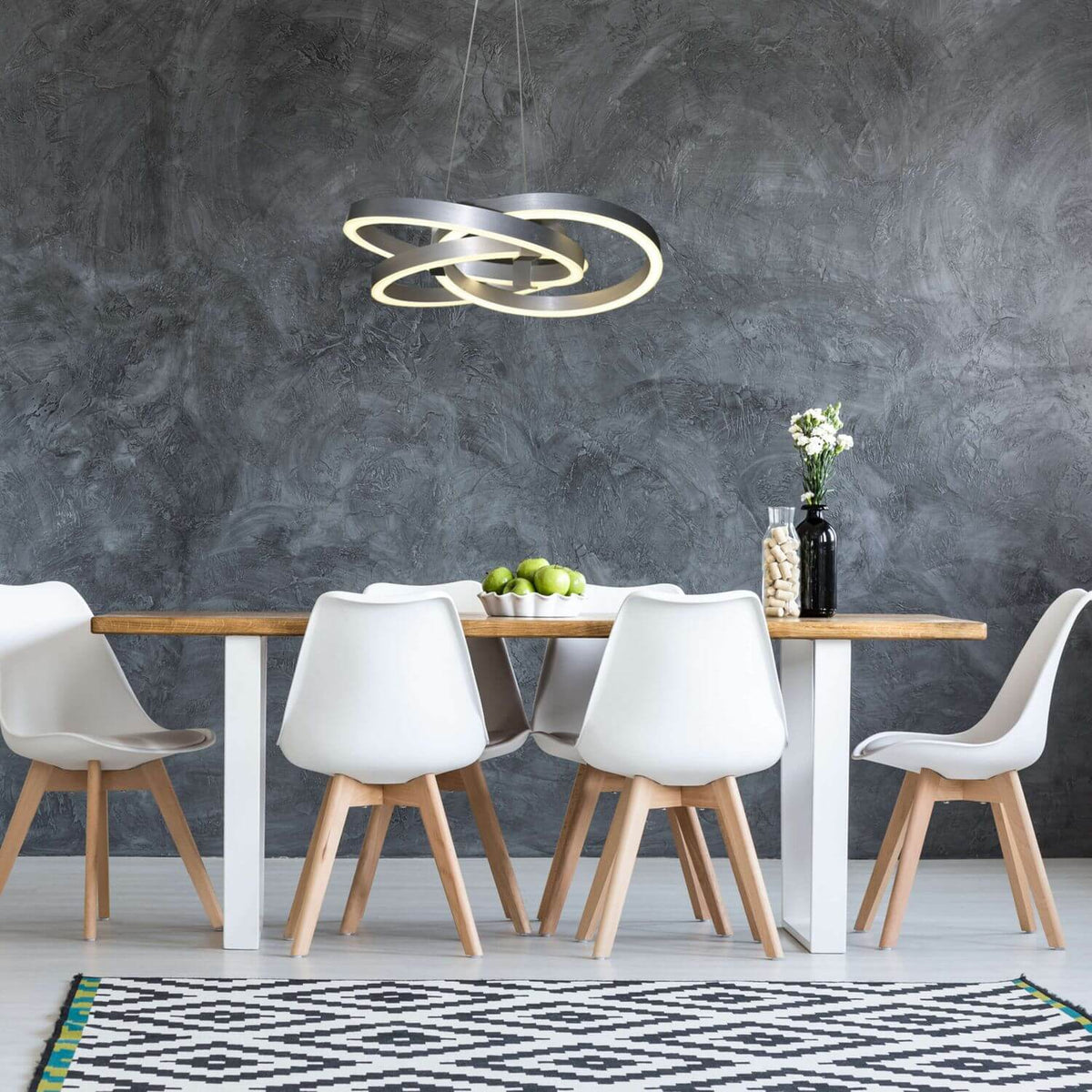 Suspension allumée au-dessus d'une table à manger, intérieur gris et chaises blanches.