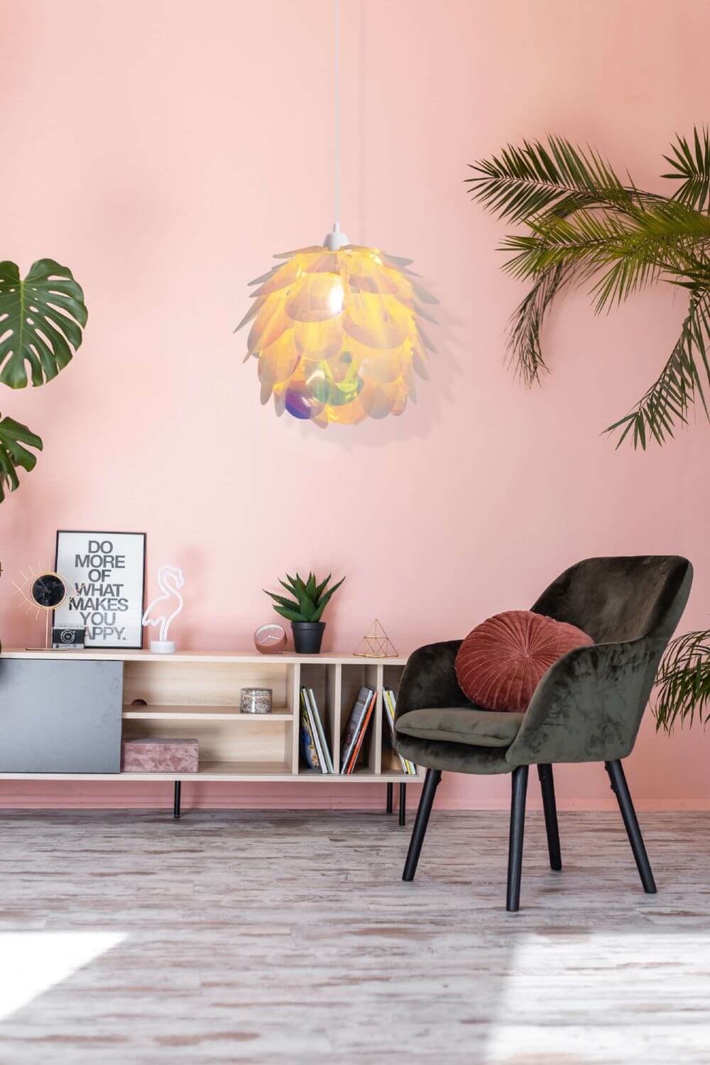Suspension aux reflets colorés dans un intérieur rose avec fauteuil vert et plantes.