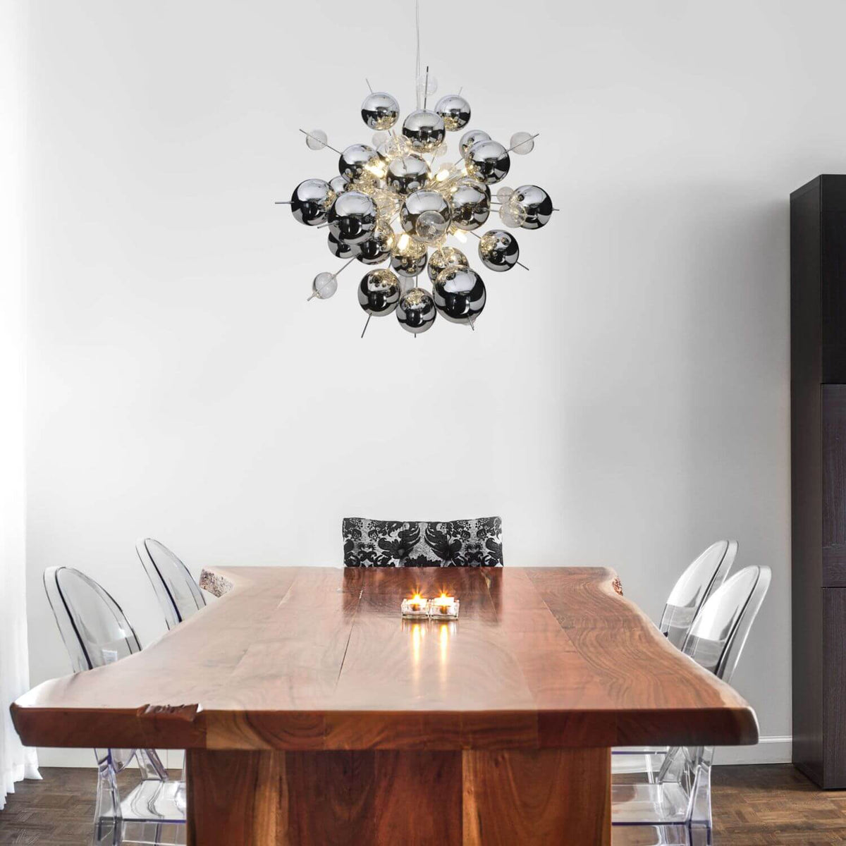 Le luminaire suspendu domine une table en bois massif entourée de chaises transparentes