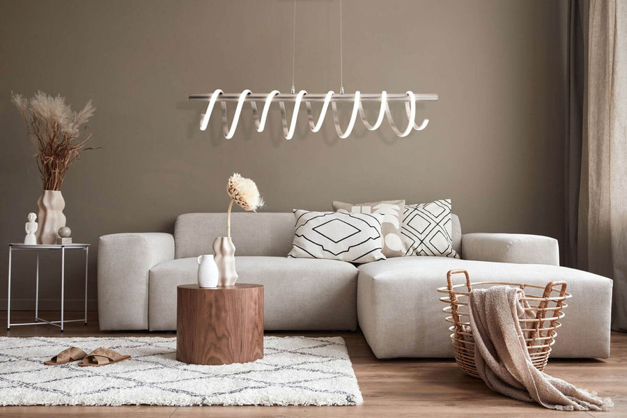 Suspension allumée dans un salon beige avec canapé d'angle et tapis.