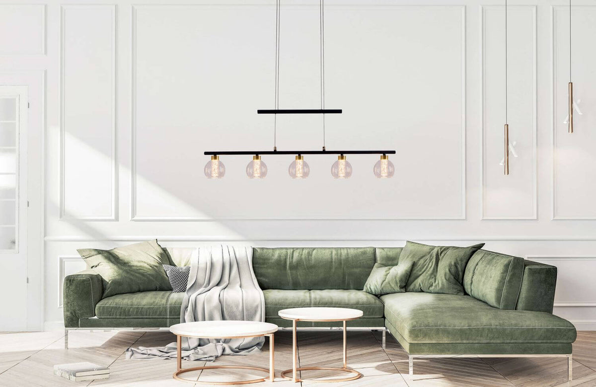 Mise en ambiance au-dessus d'un canapé vert, suspension noire et laiton allumée dans un salon.