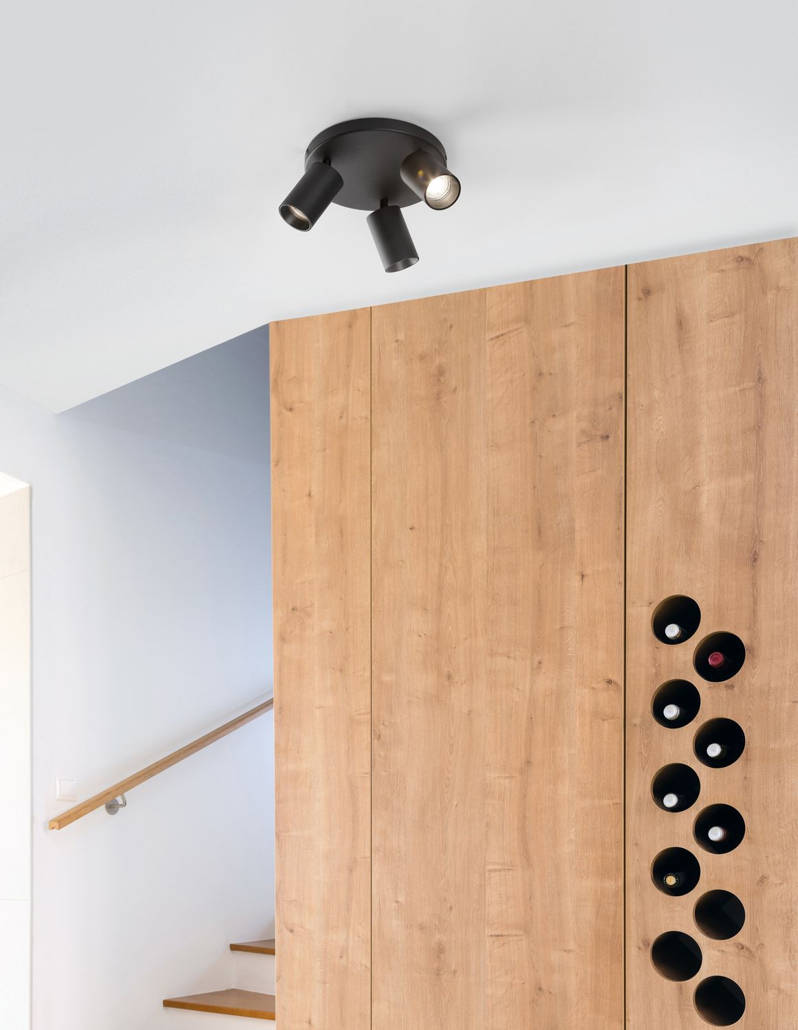 Plafonnier noir à trois spots installé au plafond devant un mur en bois clair