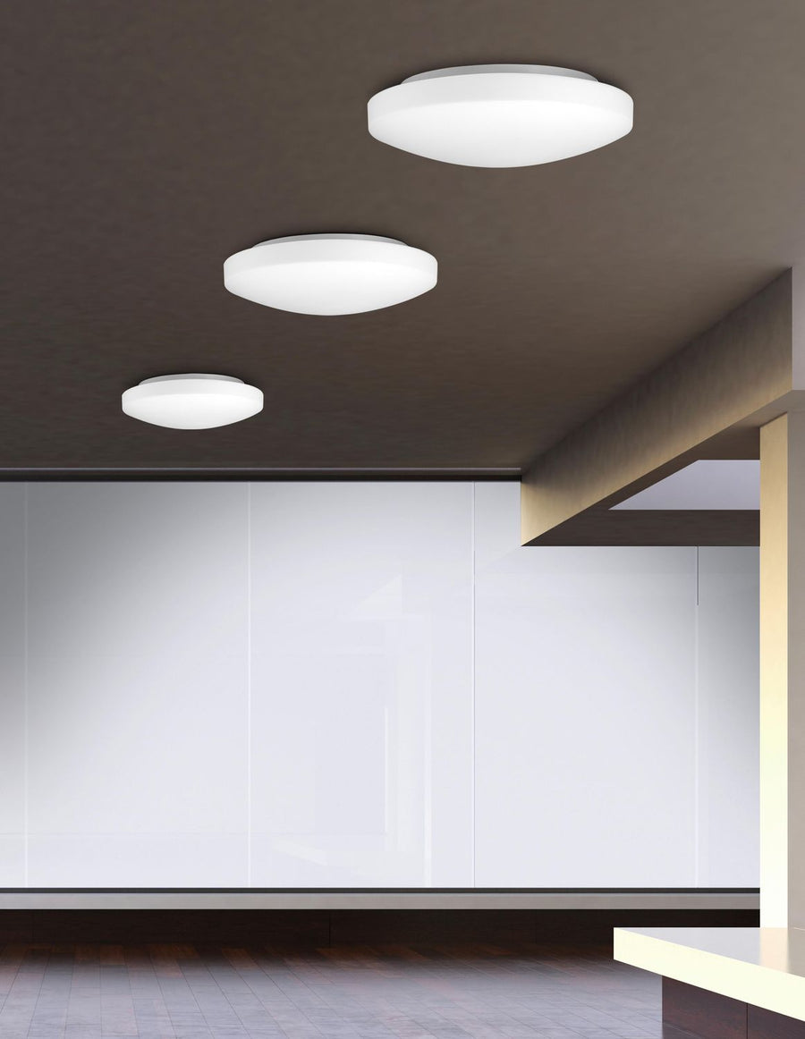 Trois plafonniers ronds blancs allumés, fixés au plafond dans un intérieur contemporain.