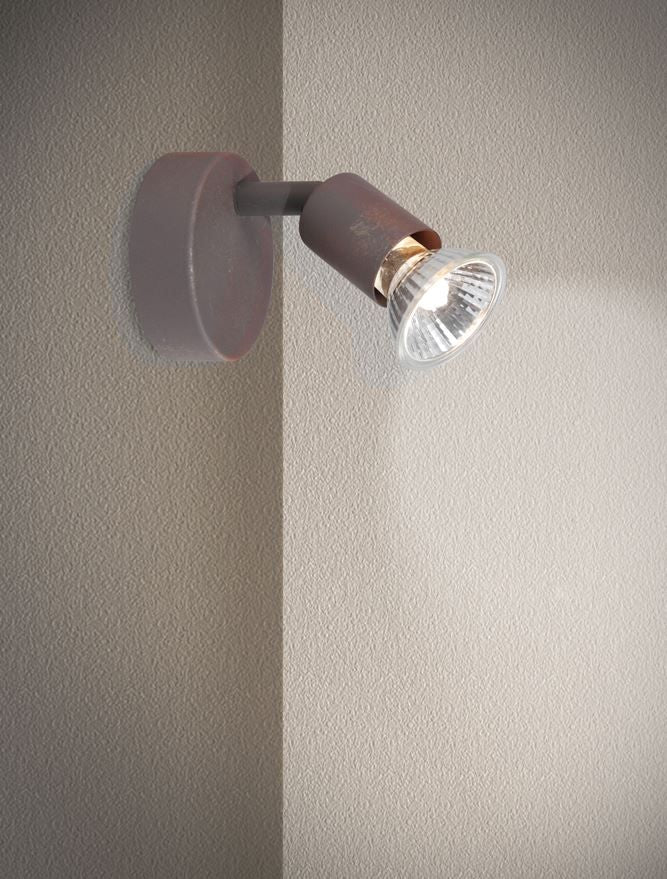 Spot orientable finition rouille allumé sur un mur beige texturé, mise en ambiance