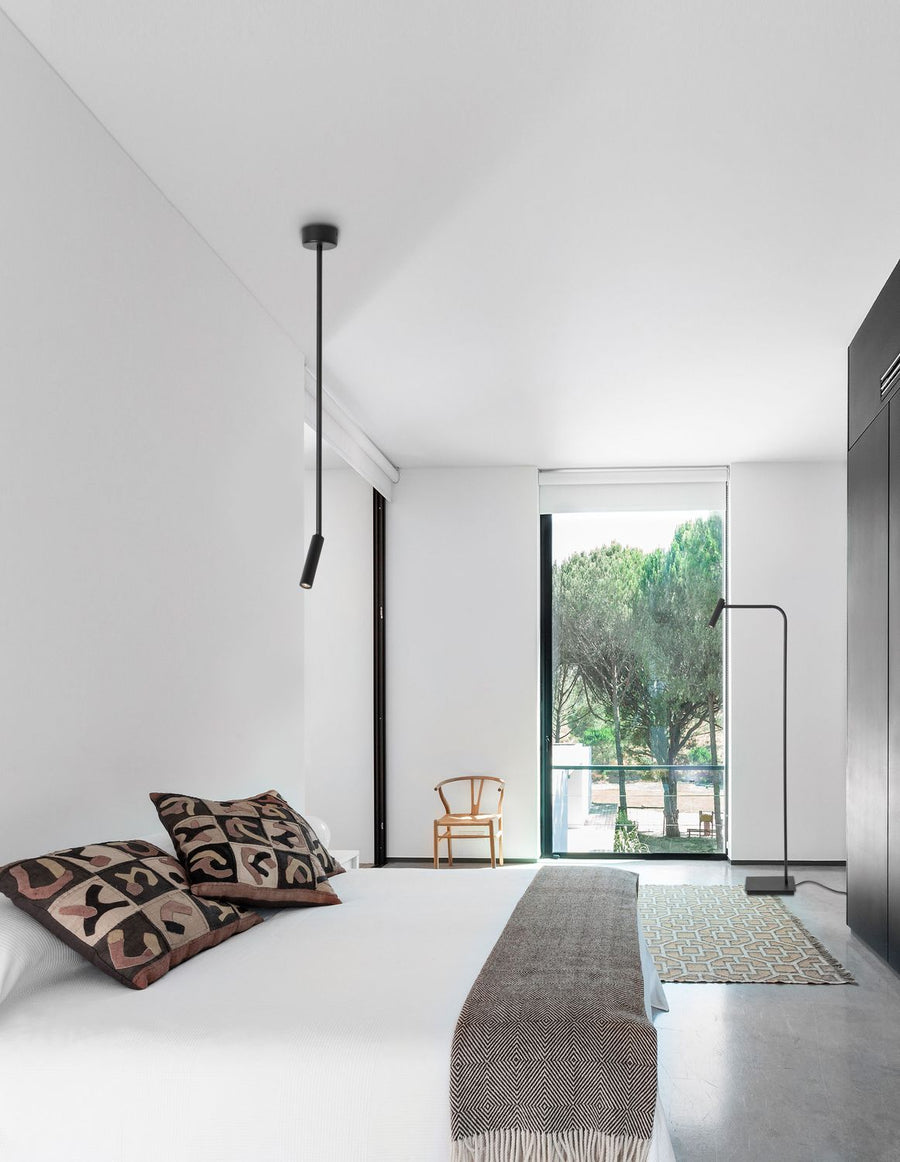 Suspension noire fine suspendue au-dessus d'un lit dans une chambre blanche minimaliste