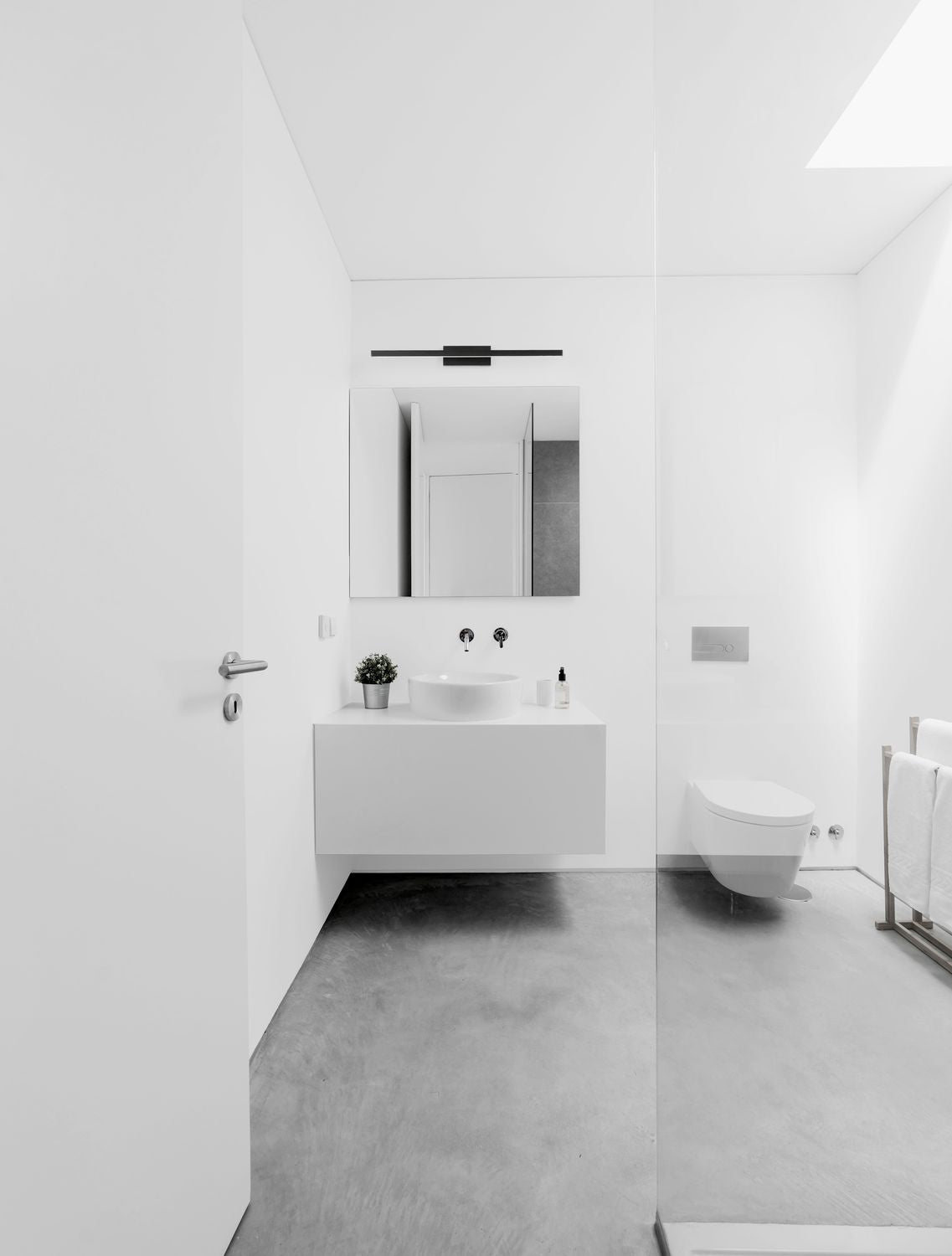 Vue d'ambiance dans une salle de bain blanche, applique noire fixée au-dessus du miroir