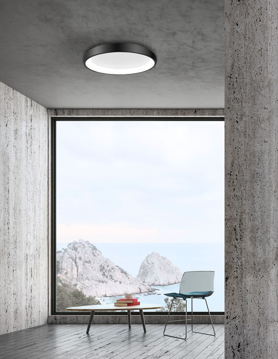 Plafonnier noir allumé au plafond d'un salon béton ouvert sur la mer