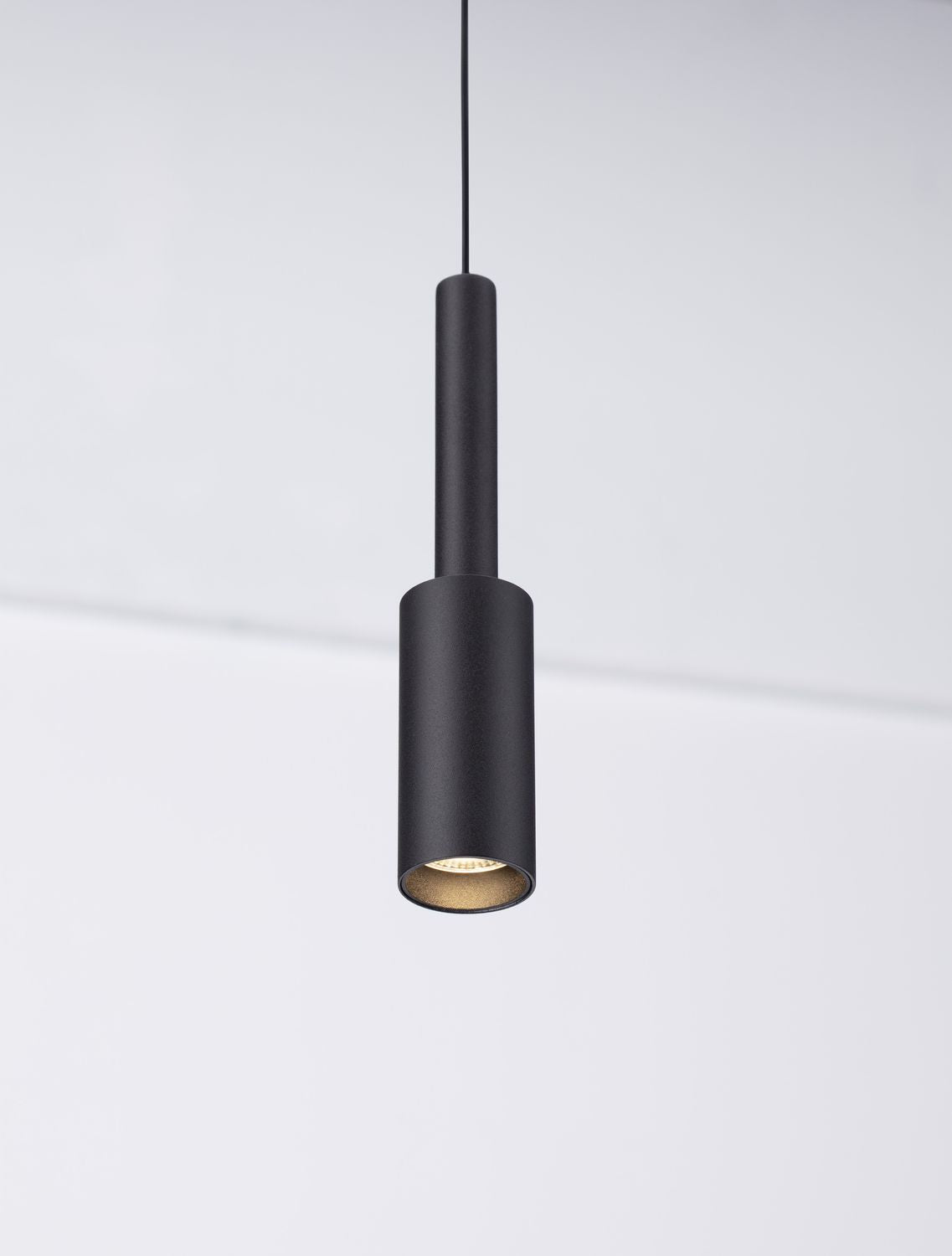 Gros plan sur le corps cylindrique noir et l'intérieur doré du luminaire