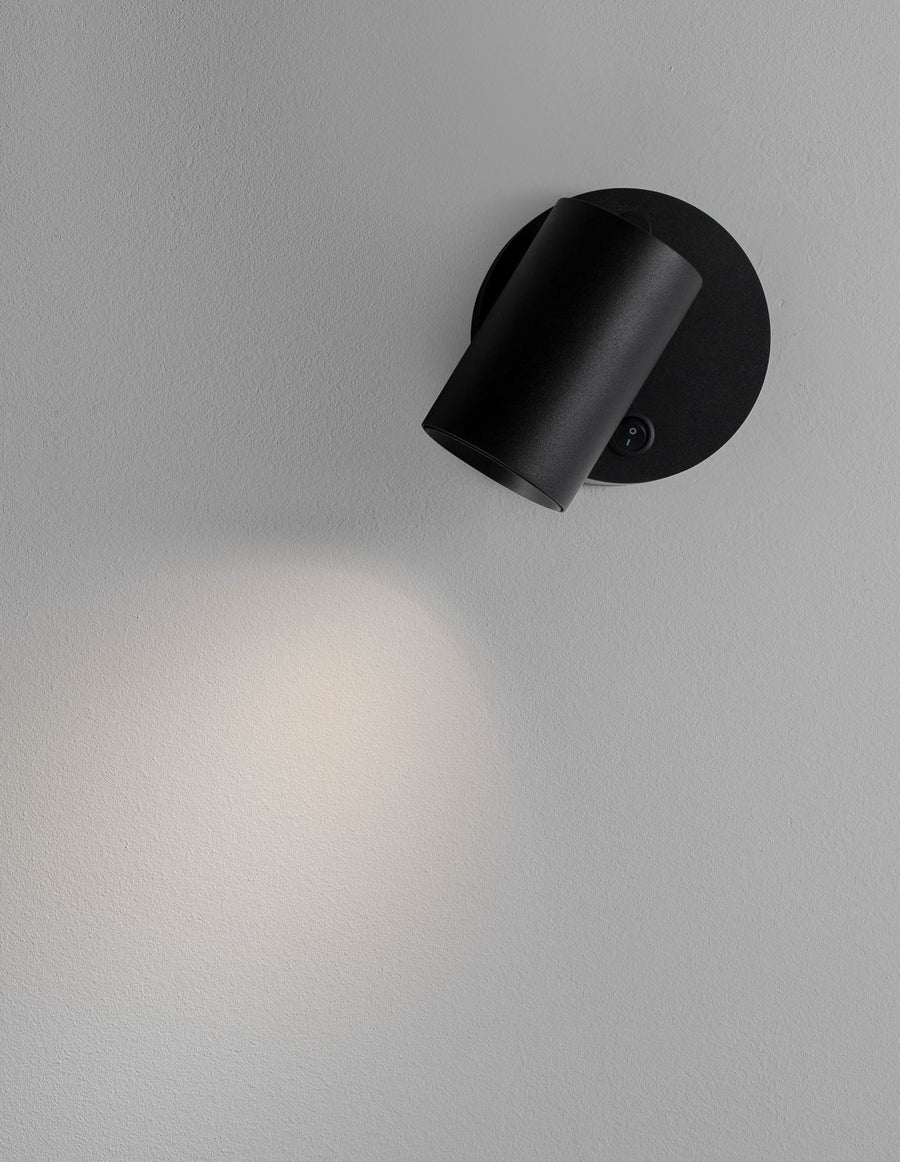 Applique noire fixée au mur, projecteur cylindrique incliné diffusant un halo lumineux