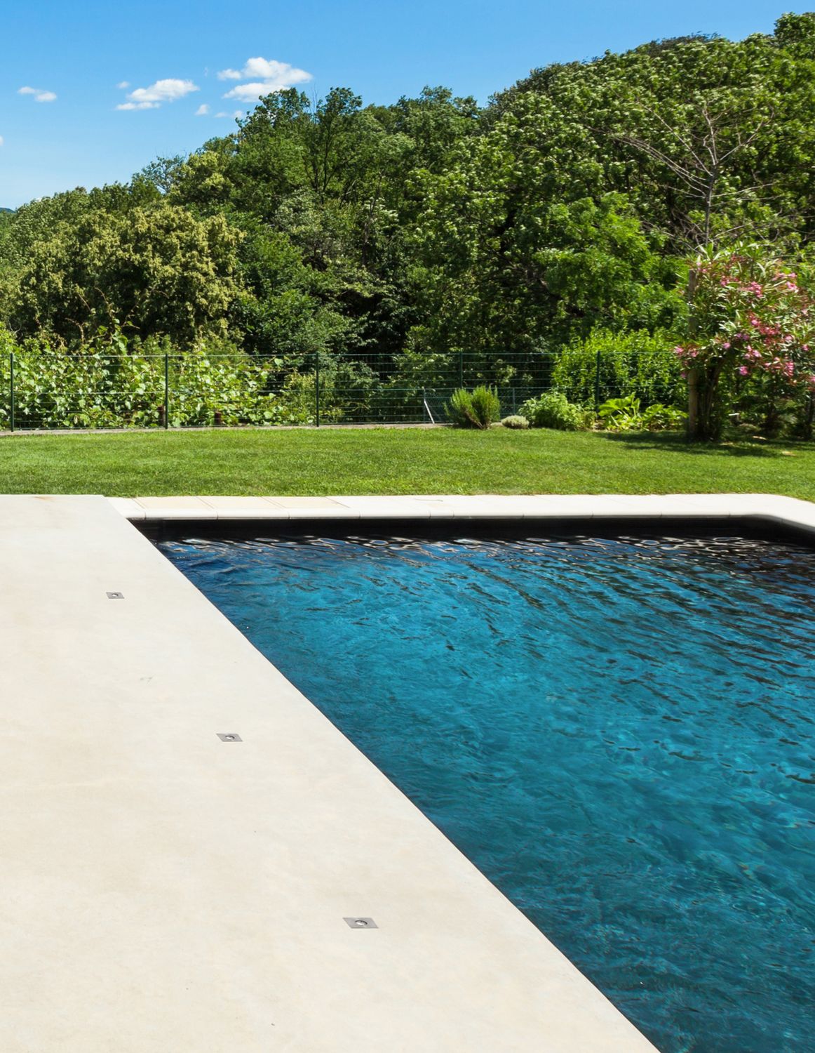 Piscine et terrasse en béton clair avec petits luminaires encastrés alignés au bord du bassin.