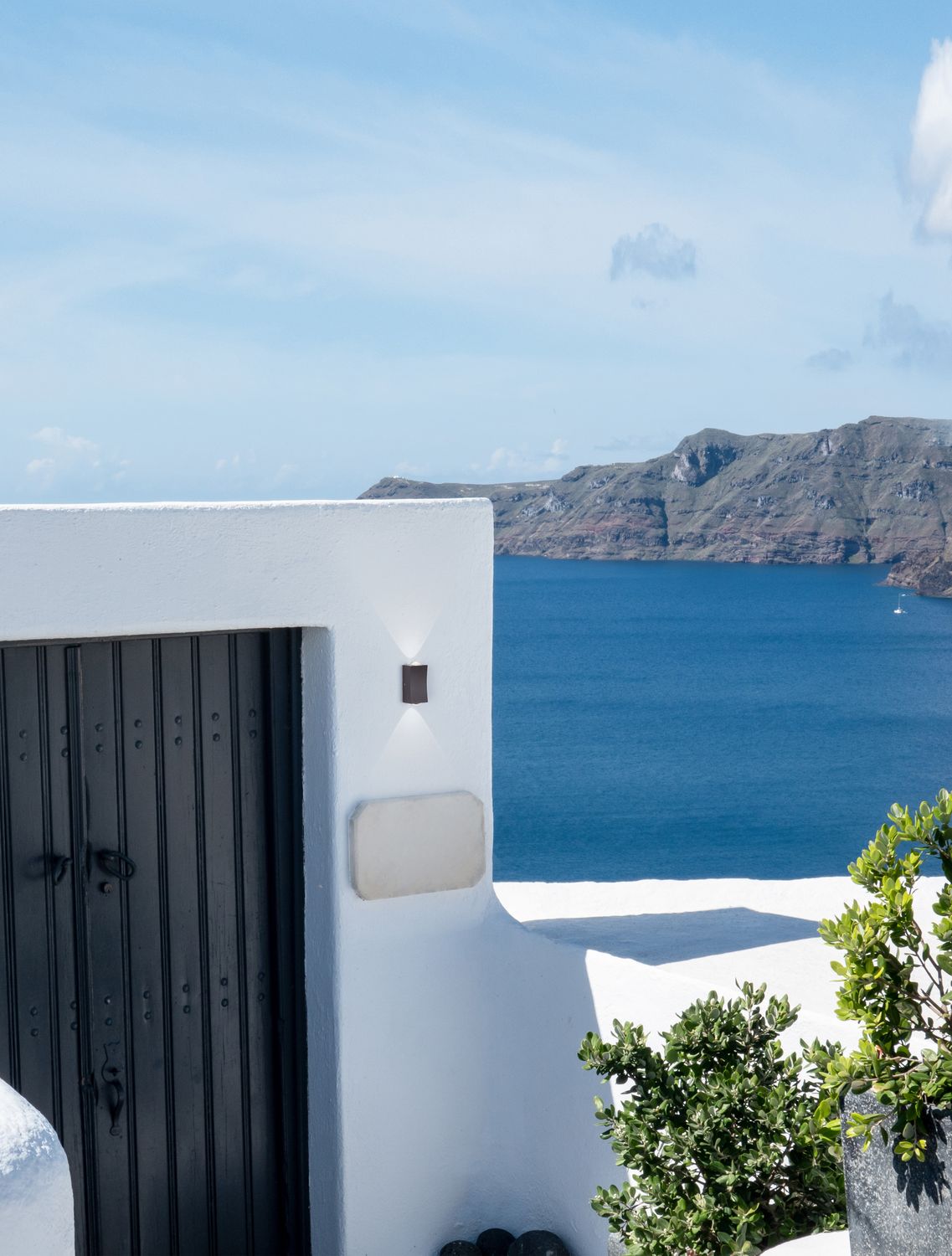 Applique murale noire allumée sur mur blanc, vue sur la mer et une île.