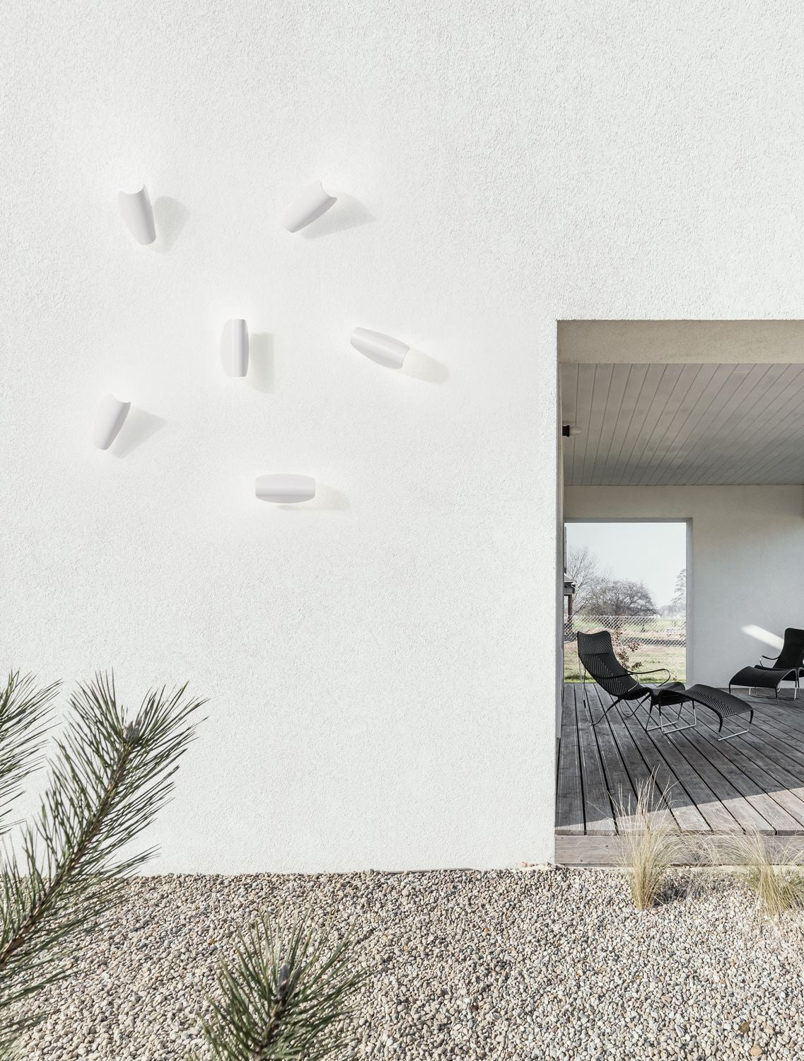 Mise en ambiance extérieure de plusieurs appliques blanches alignées sur un mur crépi, terrasse en bois