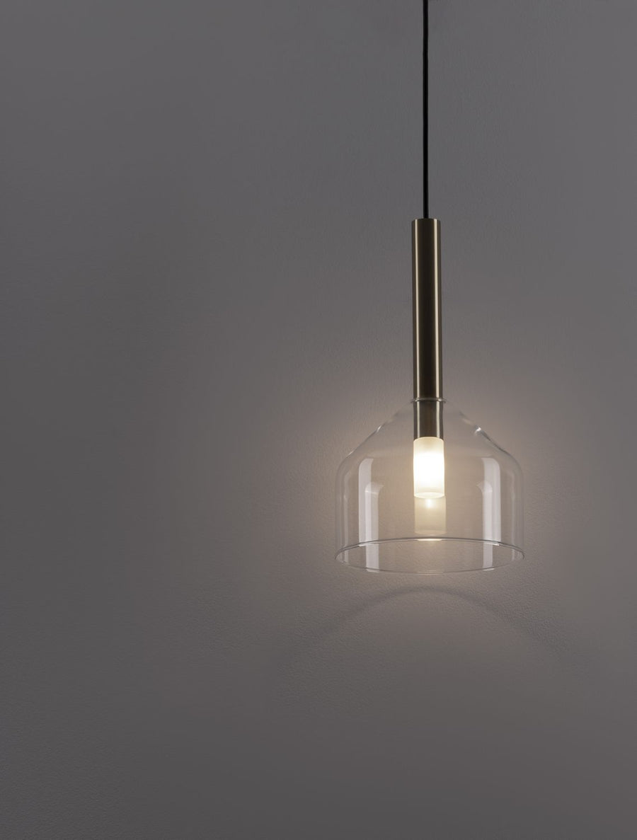Gros plan sur la suspension allumée, verre transparent et tige dorée, lumière chaude.