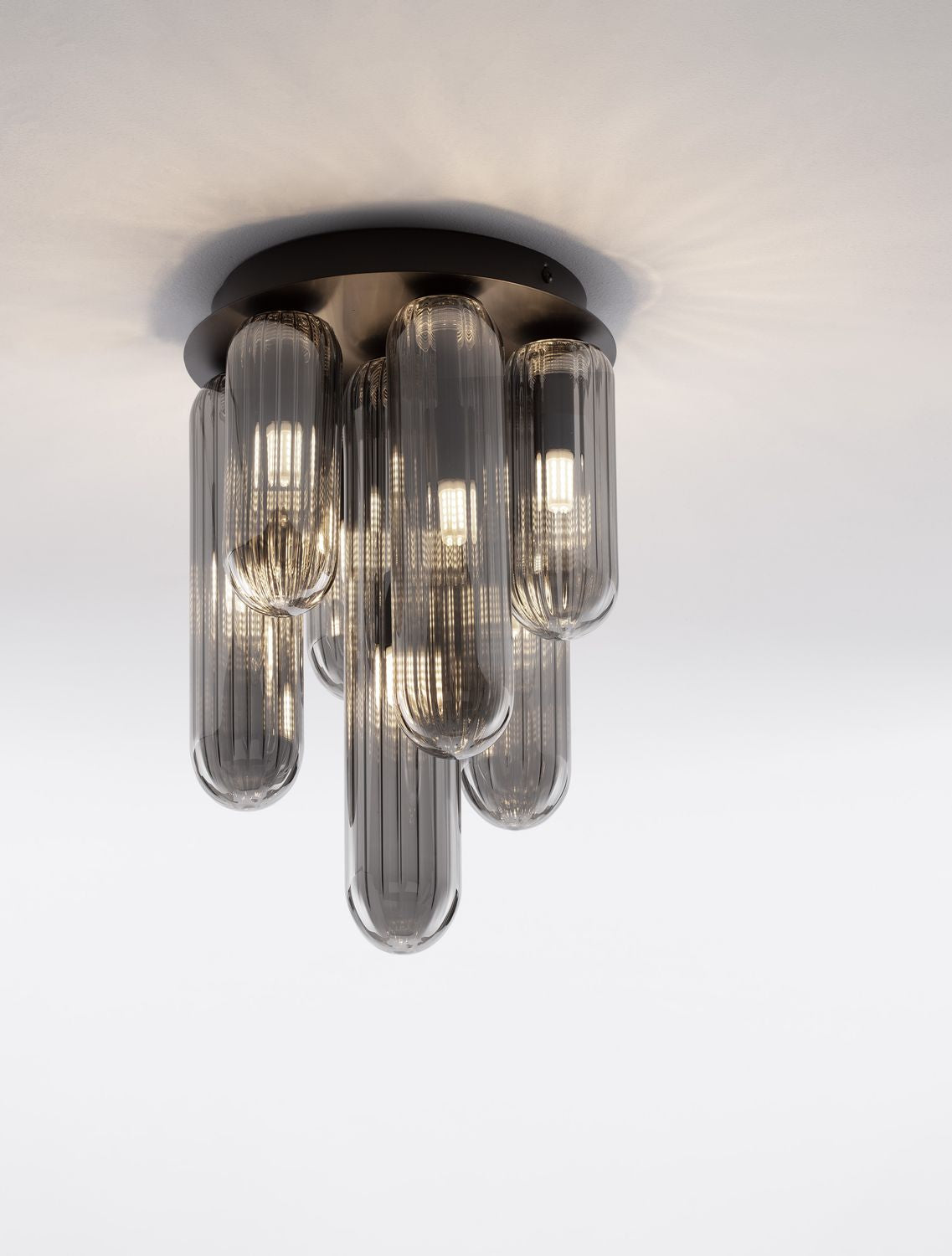 Plafonnier allumé vu de trois quarts, sept tubes de verre fumé suspendus