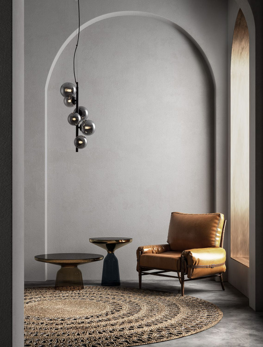 Suspension noire à six globes fumés installée dans un intérieur gris avec fauteuil en cuir.