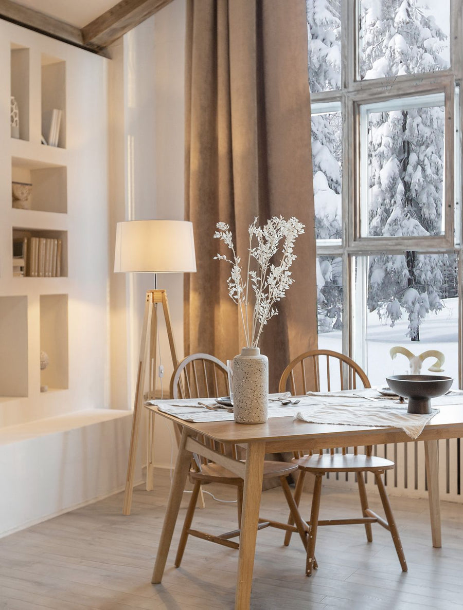 Lampadaire en bois dans une salle à manger lumineuse face à une fenêtre enneigée