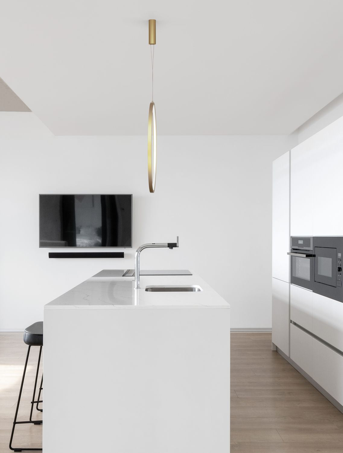 Suspension anneau doré allumée au-dessus d'un îlot de cuisine blanche contemporaine