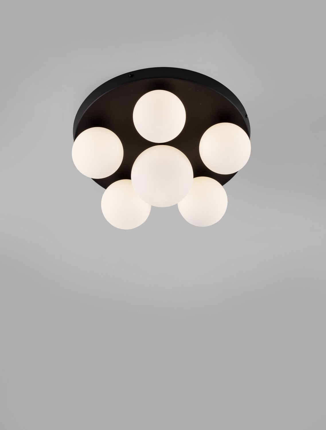 Vue de face du plafonnier allumé, six globes de verre blanc sur base ronde