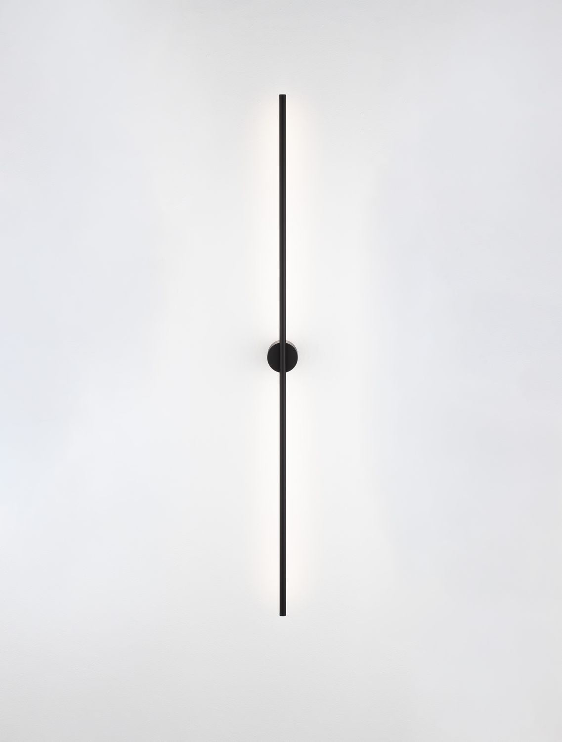Luminaire allumé diffusant un halo lumineux vertical sur le mur blanc