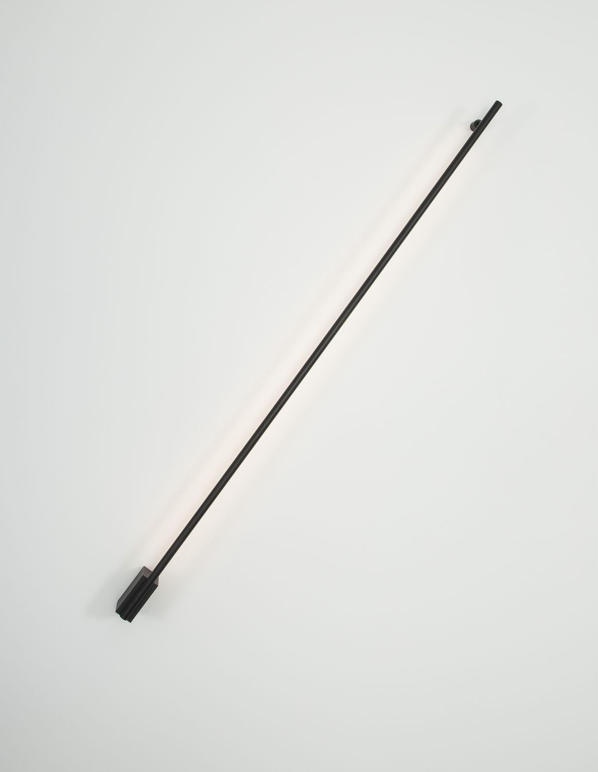 Le tube noir éclairé projette une lumière chaude contre le mur blanc