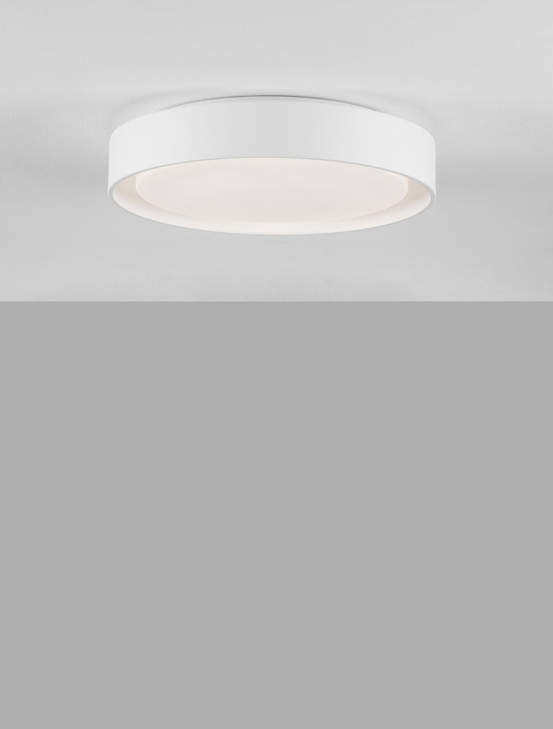 Gros plan sur le luminaire blanc rond allumé, bord cylindrique et diffuseur opale.