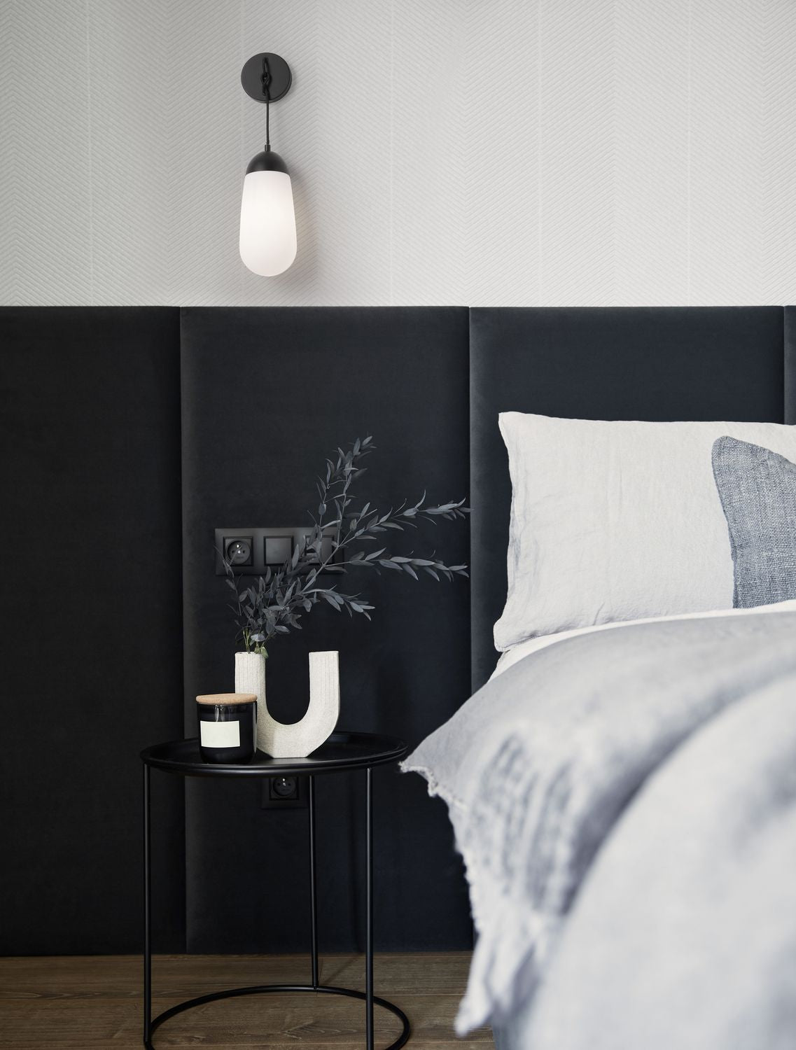 Applique murale noire allumée au-dessus d'une table de chevet dans une chambre sombre
