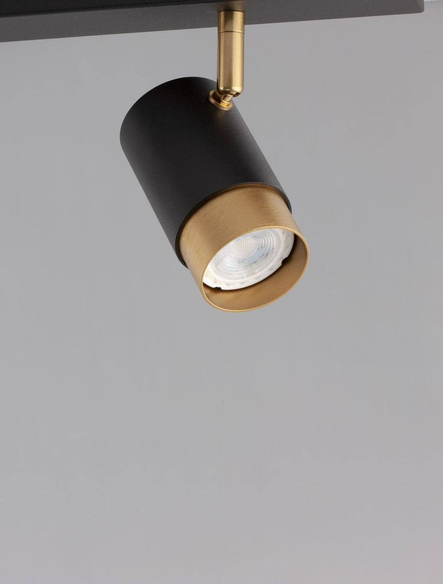 Détail rapproché d'un spot : corps noir mat, collerette dorée, ampoule LED