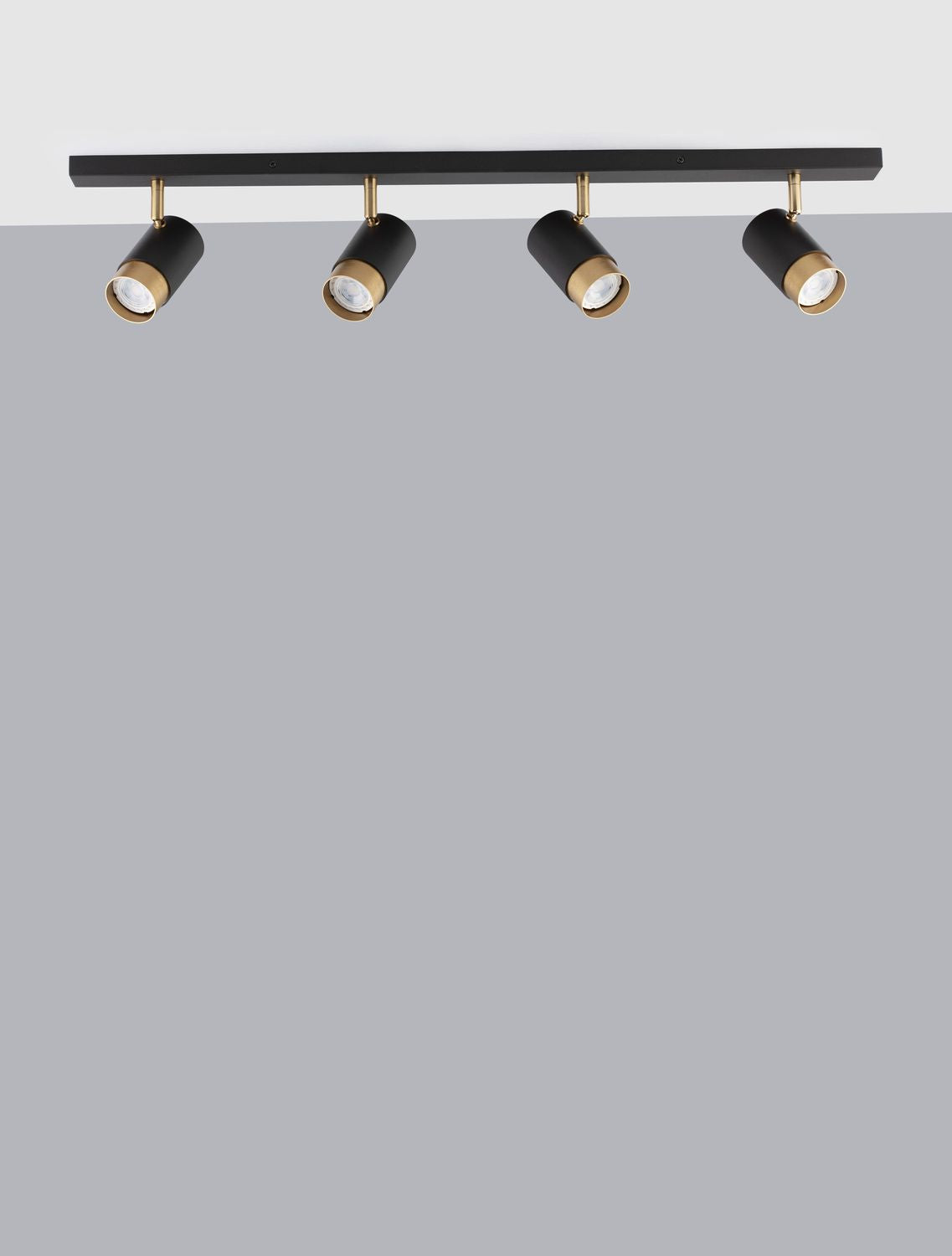 Vue de face sur fond gris du luminaire noir à quatre spots dorés fixés sur rail.